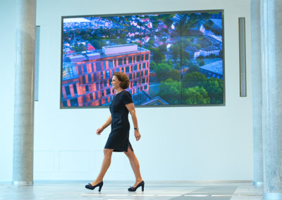 Helen Hain läuft durch ein Foyer mit Displayhintergrund